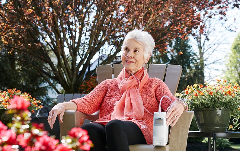 Older woman sitting outside relaxing with her portable G4 oxygen device.